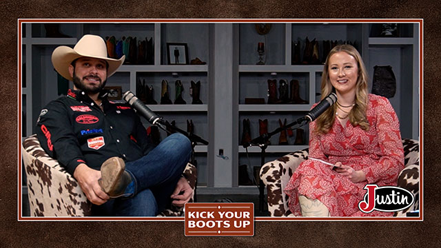 A woman with blonde hair and a man with black hair wearing a cowboy hat, looking at the camera, smiling, and sitting in chairs having a conversation.